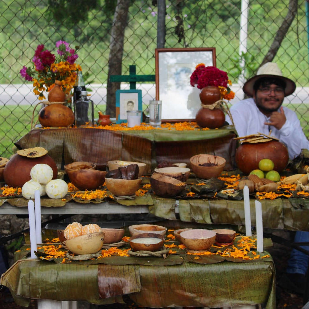 Man sitting at a table with a traditional offering for Hanal Pixan celebration.