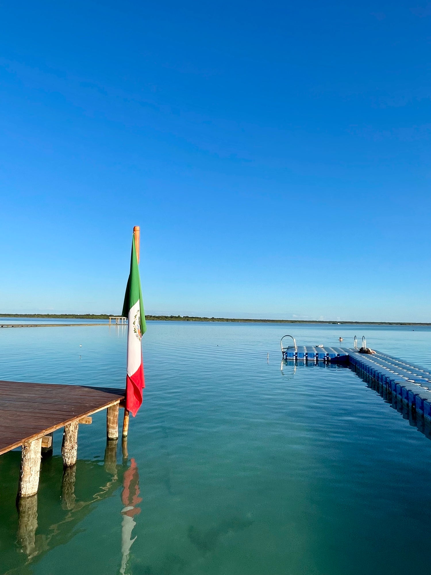 Bacalar Lagoon of Seven Colors with a wooden dock and the Mexican flag, Crossing Yucatán journey